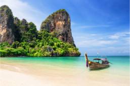 Beach with clear water and traditional boat near rocky cliffs