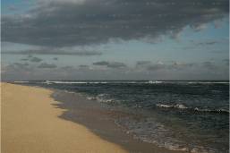 Sandy beach with ocean waves under a cloudy sky