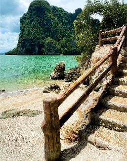 Stone steps with wooden railing lead down to a beach area