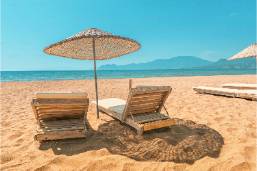 Two wooden lounge chairs under a straw umbrella on the beach