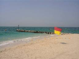 Sandy beach with a wooden pier and a lifeguard flag