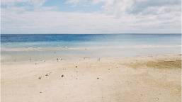 Wide sandy beach area with gentle ocean waves under cloudy sky