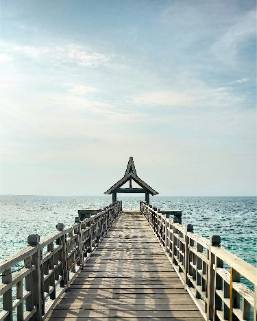 Wooden pier extending over ocean water under a partly cloudy sky