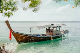 Wooden boat floating near tropical beach with clear water