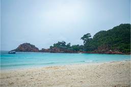 Sandy beach with calm ocean and green hillside in background
