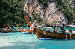 Traditional boats docked at a clear water beach near cliffs