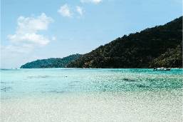 Clear ocean water with sandy beach and hillside in background