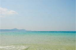 Clear ocean water with a distant shoreline and calm sky