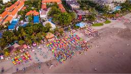 A crowded beach with colorful umbrellas near a hotel area