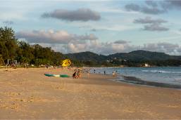 Wide sandy beach with calm waves and distant hills.