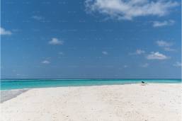 Wide sandy beach with clear blue ocean and sky